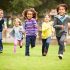 Group Of Young Children Running Towards Camera In Park Smiling To Camera